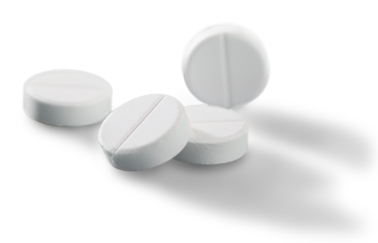 Close-up of four white, round tablets with a scored line across the center, resting on a white background with soft shadows.