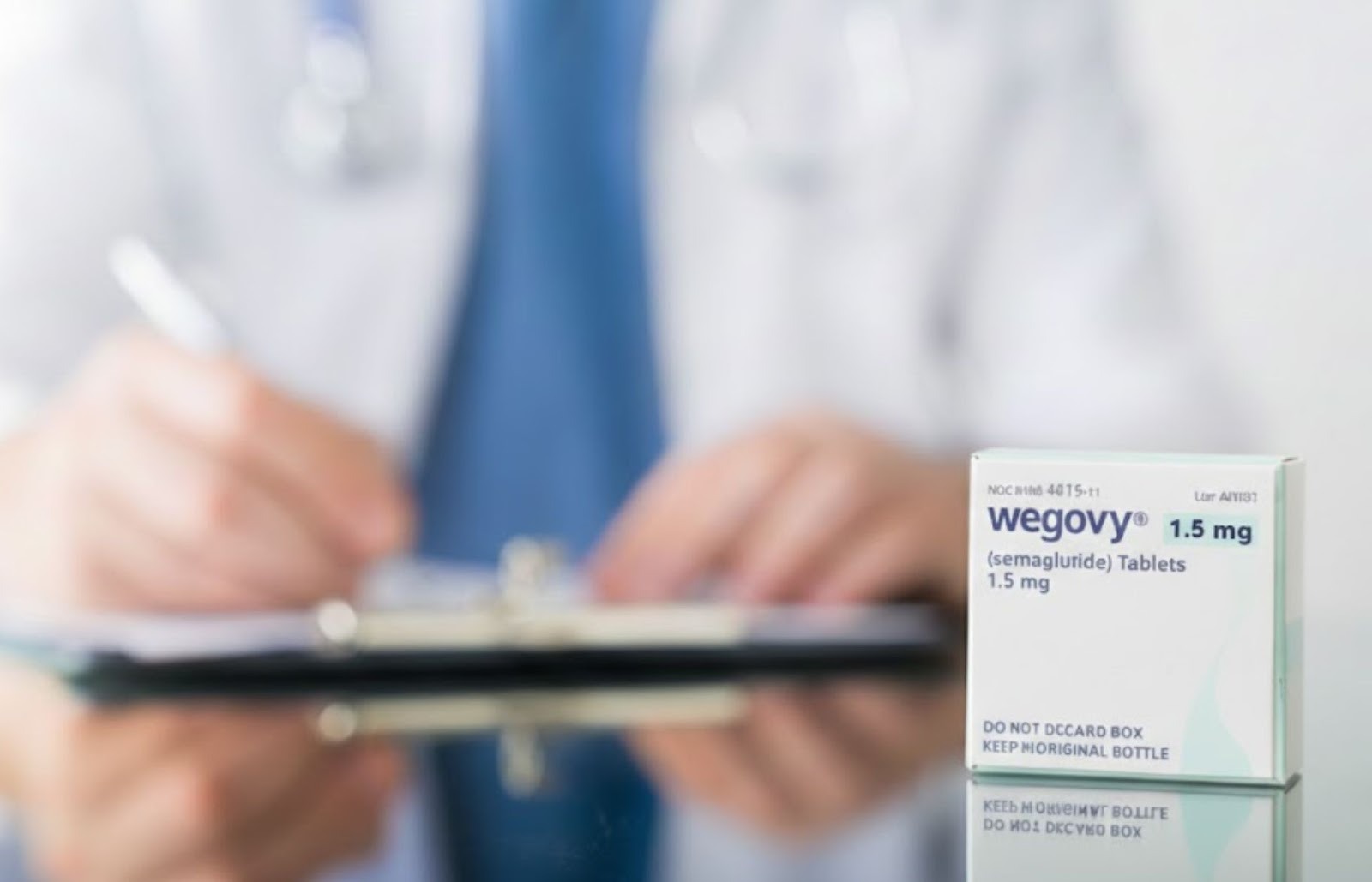 A box of Wegovy 1.5 mg semaglutide tablets in sharp focus on a desk, with a blurred healthcare professional in a white coat writing on a clipboard in the background.