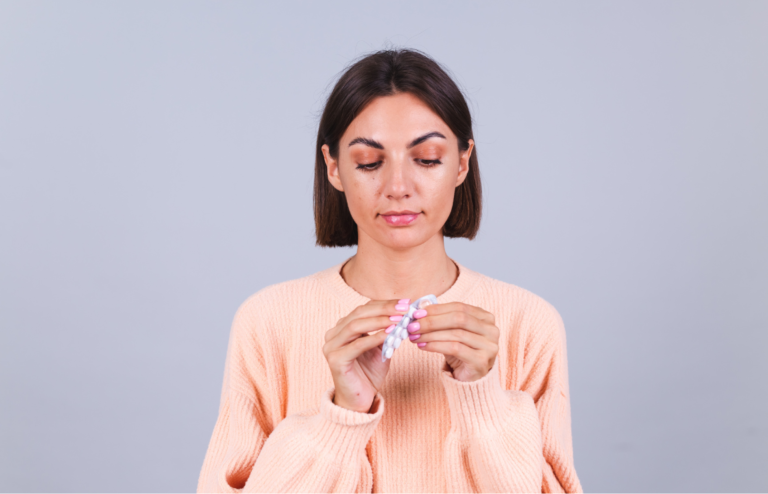 Woman in a peach sweater looking down at a blister pack of pills