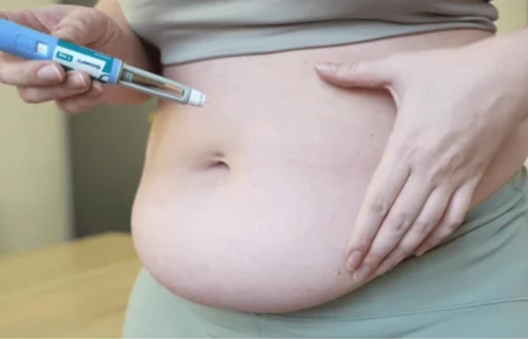 Close-up of a person’s abdomen as they administer a subcutaneous injection using a pen device.