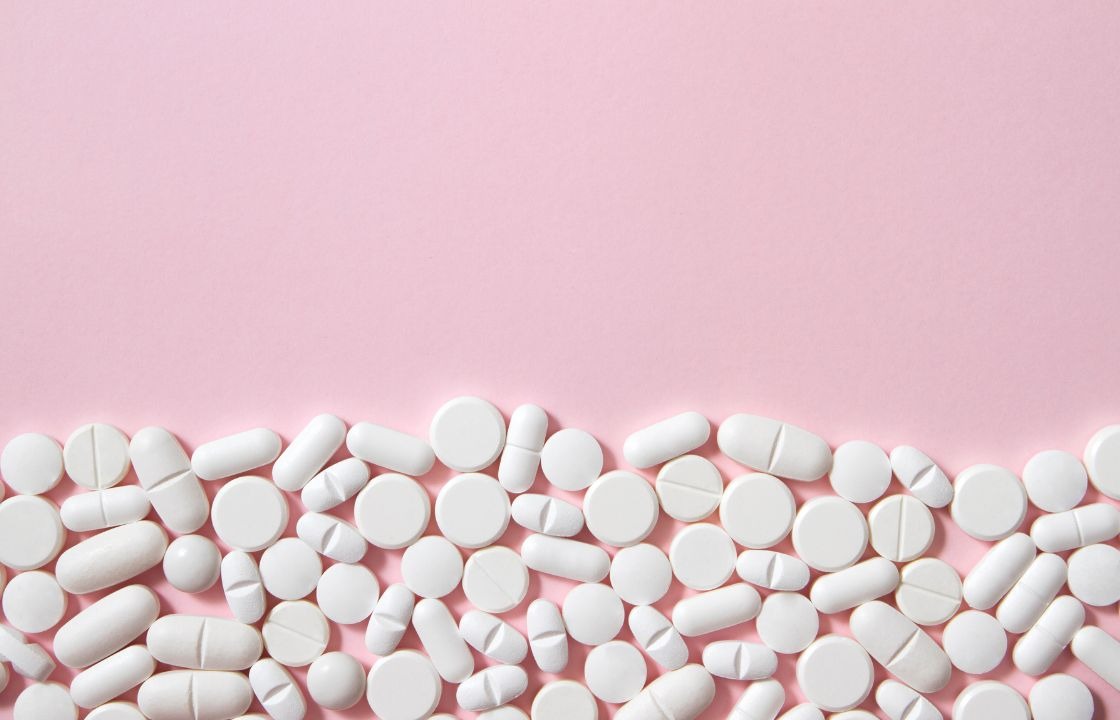 White prescription pills and tablets on a pink background representing GLP-1 pills and phentermine weight loss medications