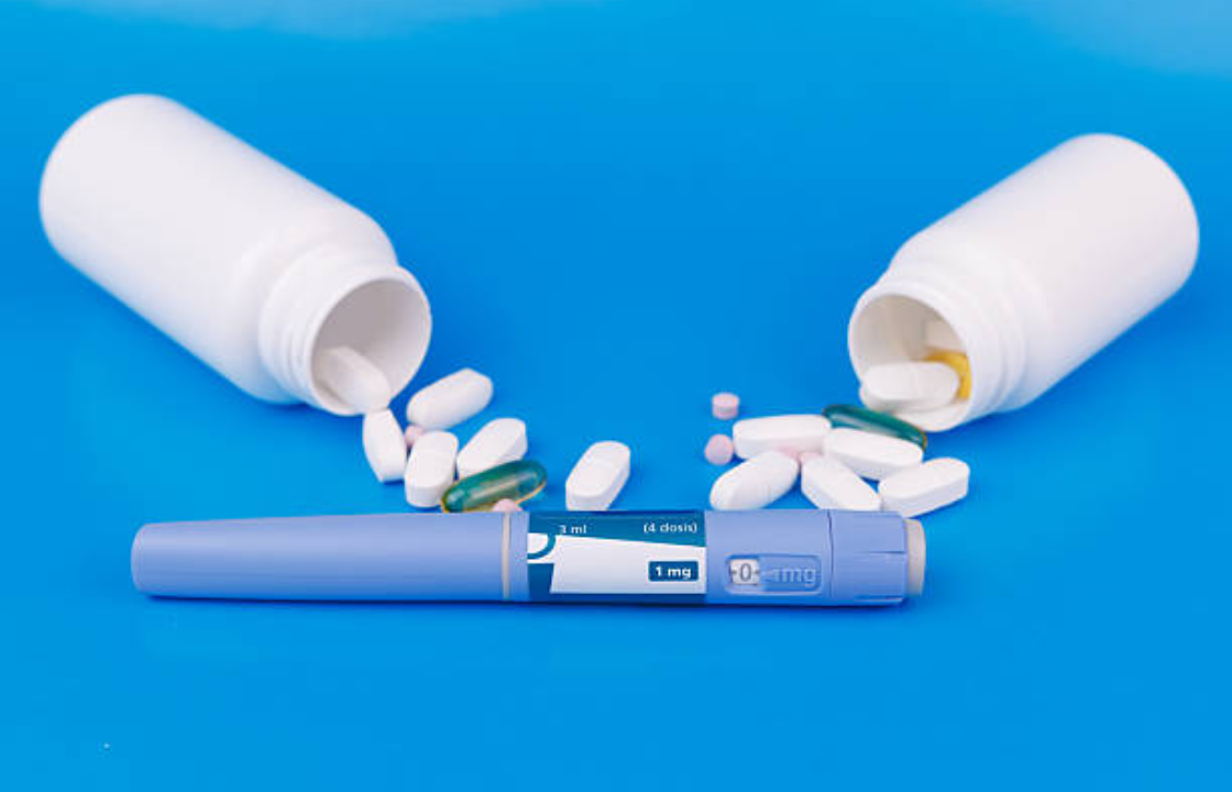 GLP-1 weight loss injection pen with spilled pills from two white medicine bottles on a blue background.