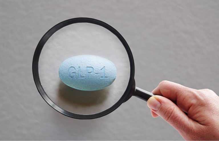 Magnifying glass focusing on a blue GLP-1 pill on a plain background.