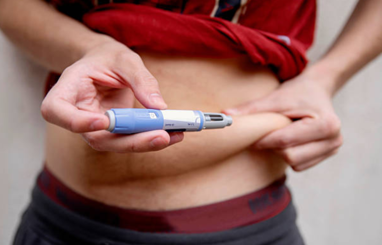 Person injecting medication into abdomen using a pen device.