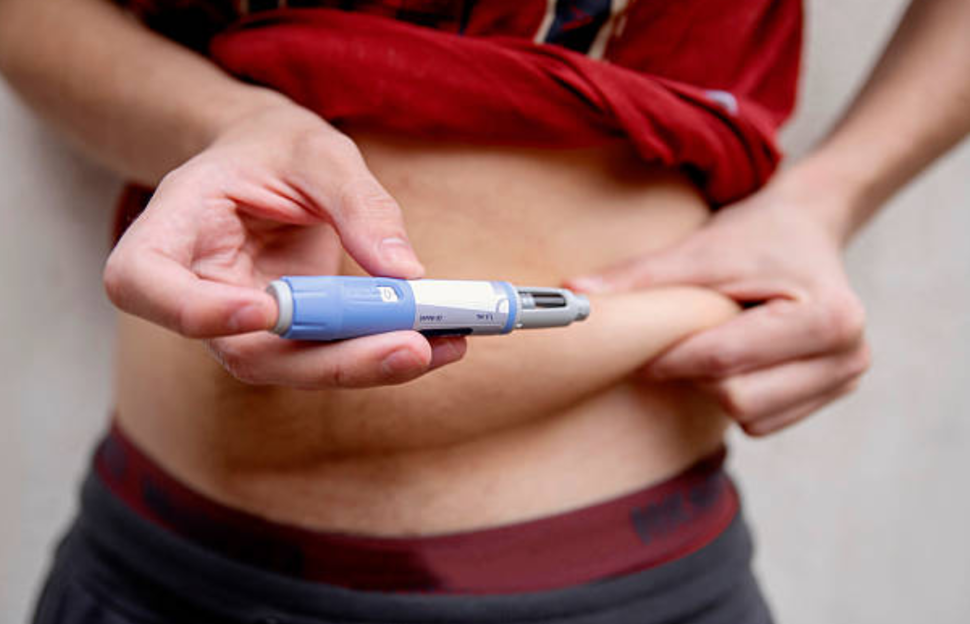 Person injecting medication into abdomen using a pen device.