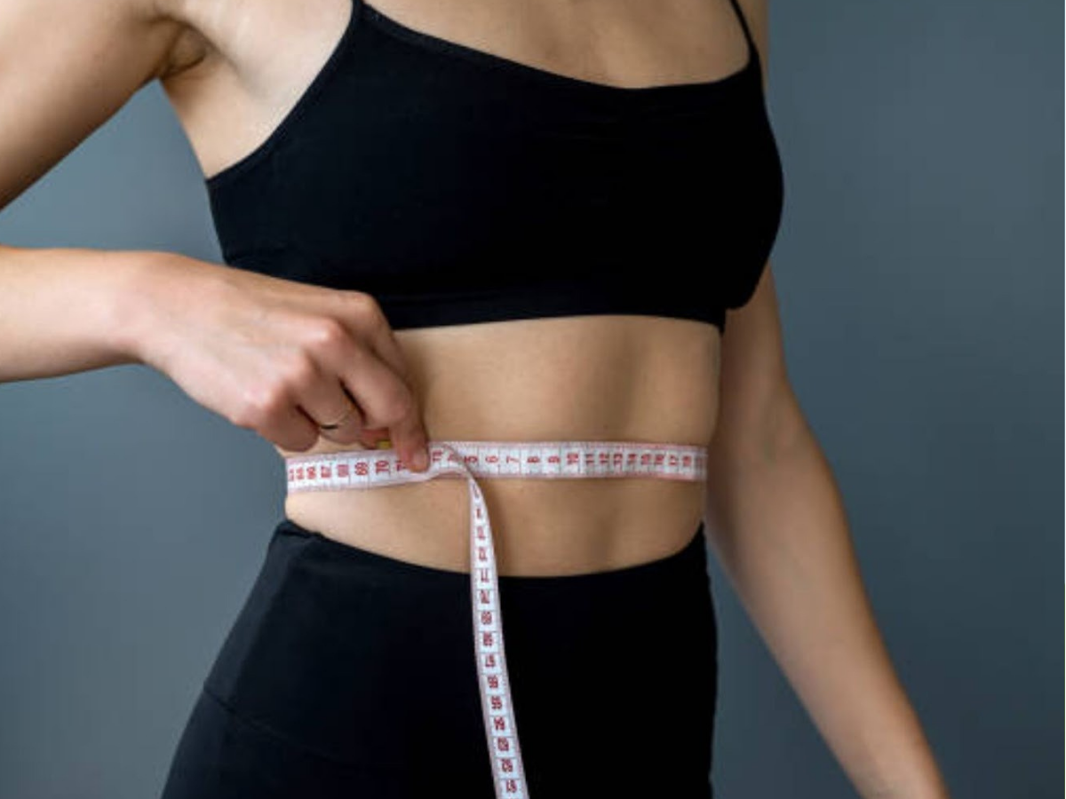 Woman measuring waist with tape to track weight loss progress