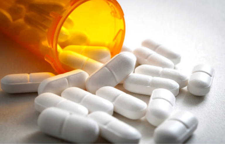White oral medication tablets spilling from a prescription pill bottle.