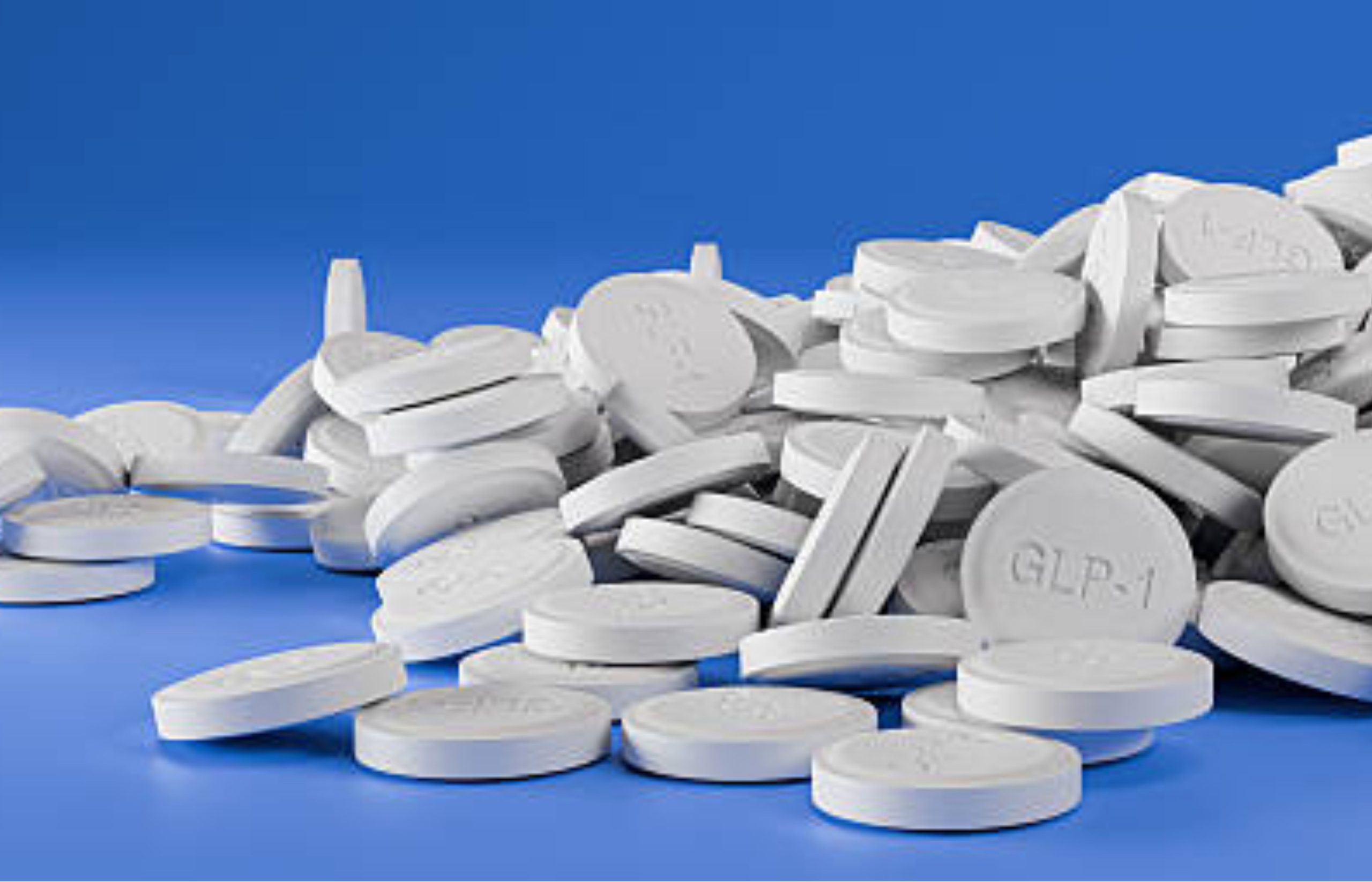 White GLP-1 tablets scattered on a blue background, representing oral diabetes medication.