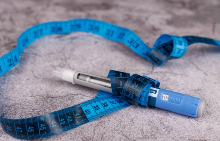 GLP-1 weight loss injection pen placed on a surface with a blue measuring tape symbolizing obesity treatment and weight management.