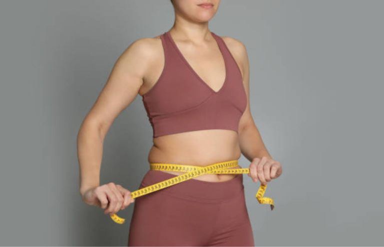 Woman measuring waist with a tape, representing weight loss and obesity treatment progress