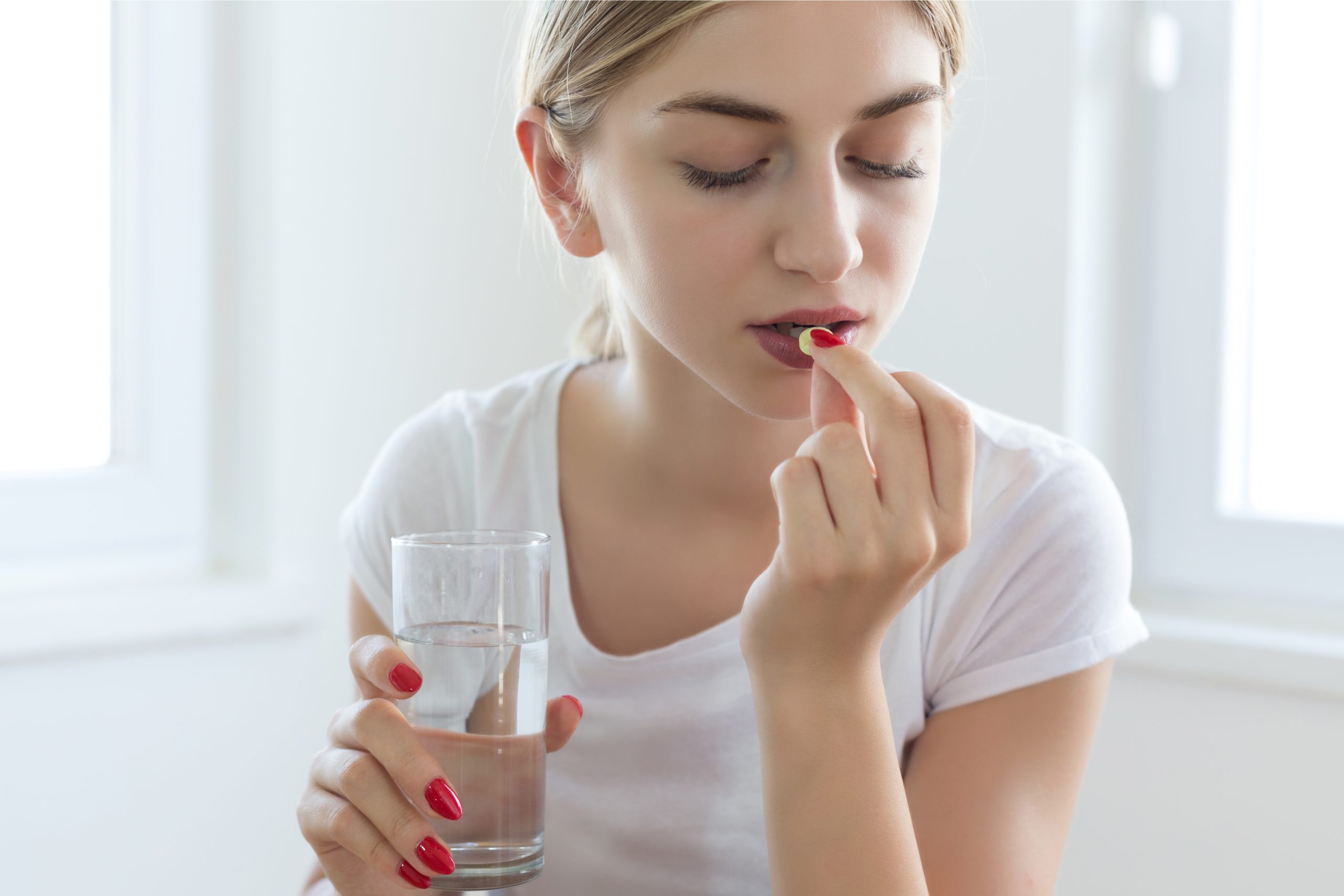 Woman taking a weight loss pill with a glass of water, representing daily oral GLP-1 medication for obesity or diabetes treatment.