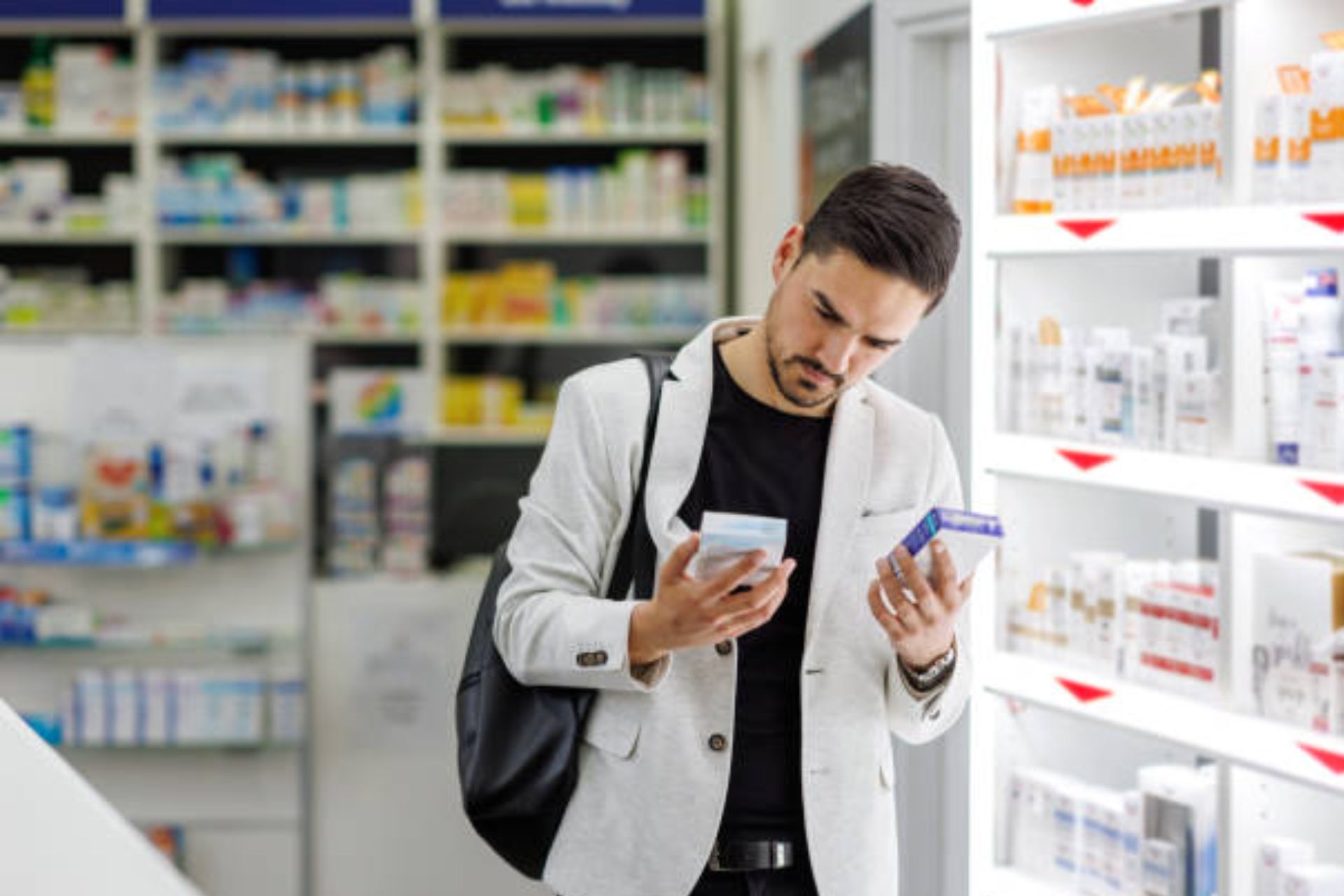 Man comparing medication boxes in a pharmacy aisle.