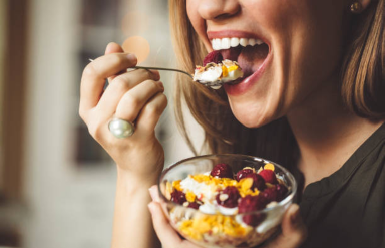 Person eating a bowl of yogurt topped with berries and cereal using a spoon.