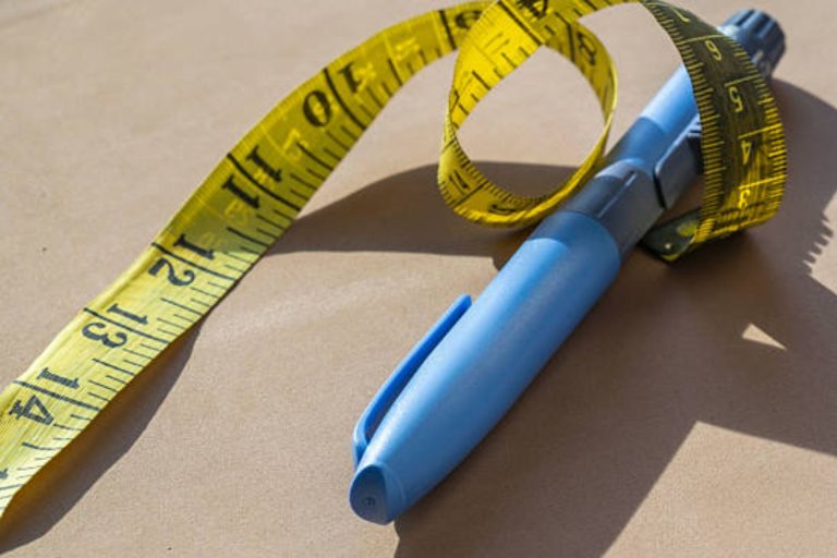 Blue injection pen beside a yellow measuring tape on a surface