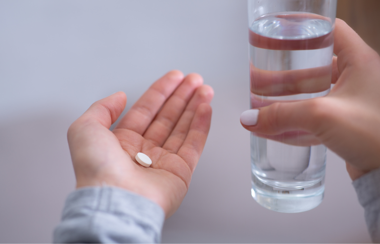 Hand holding a pill with a glass of water ready to take medication.