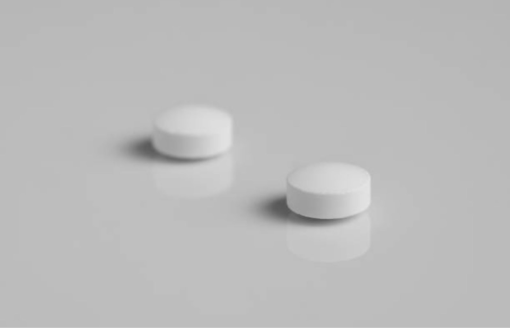 Two white round tablets placed on a clean, light grey surface with soft shadows.