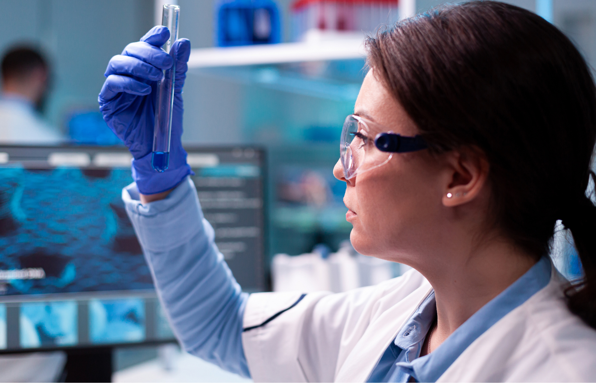 Scientist wearing safety goggles examines a test tube with blue liquid in a lab.