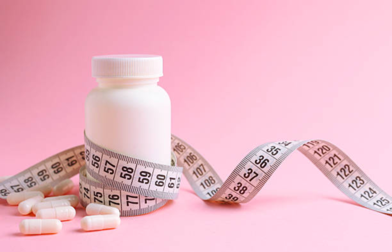 Weight loss pills bottle with measuring tape on pink background