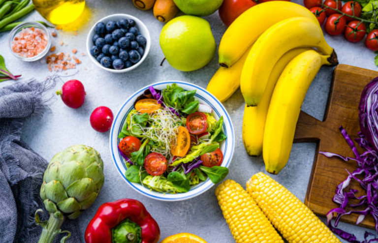 Colorful assortment of fresh fruits and vegetables with a bowl of salad, bananas, corn, blueberries, and leafy greens.
