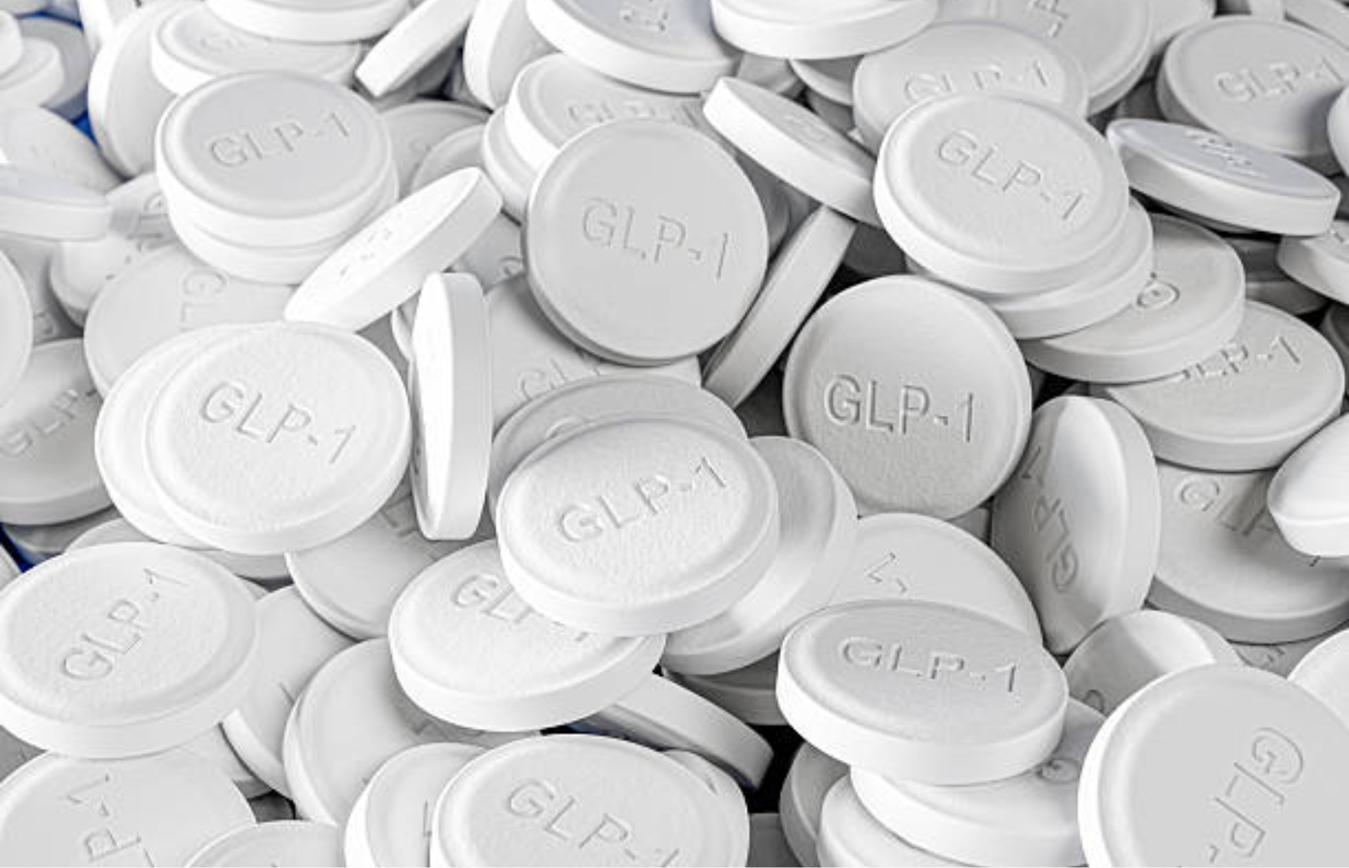 Close-up of multiple white tablets labeled “GLP-1,” representing oral weight management medication.