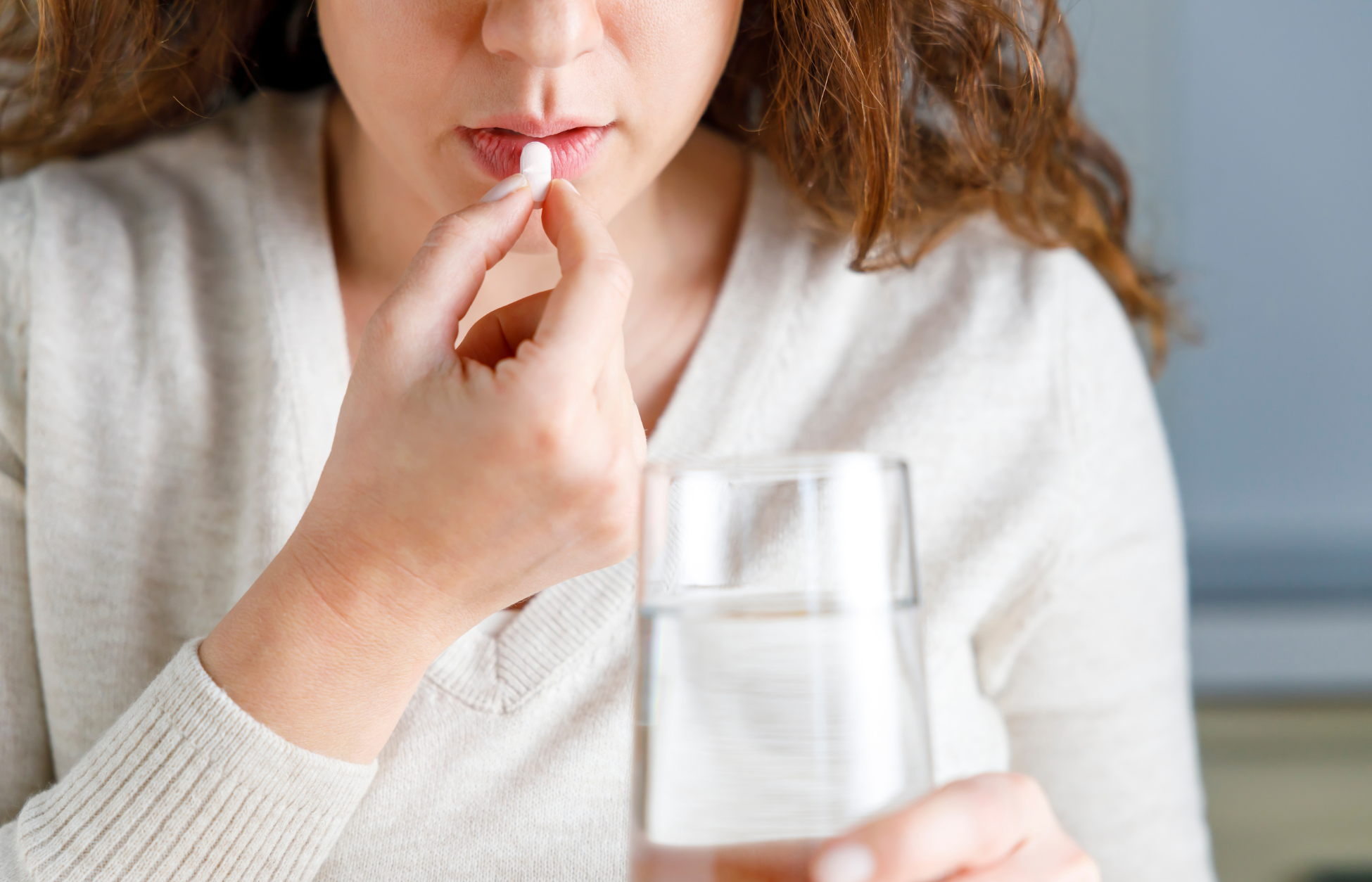 Person taking a pill with a glass of water at a table