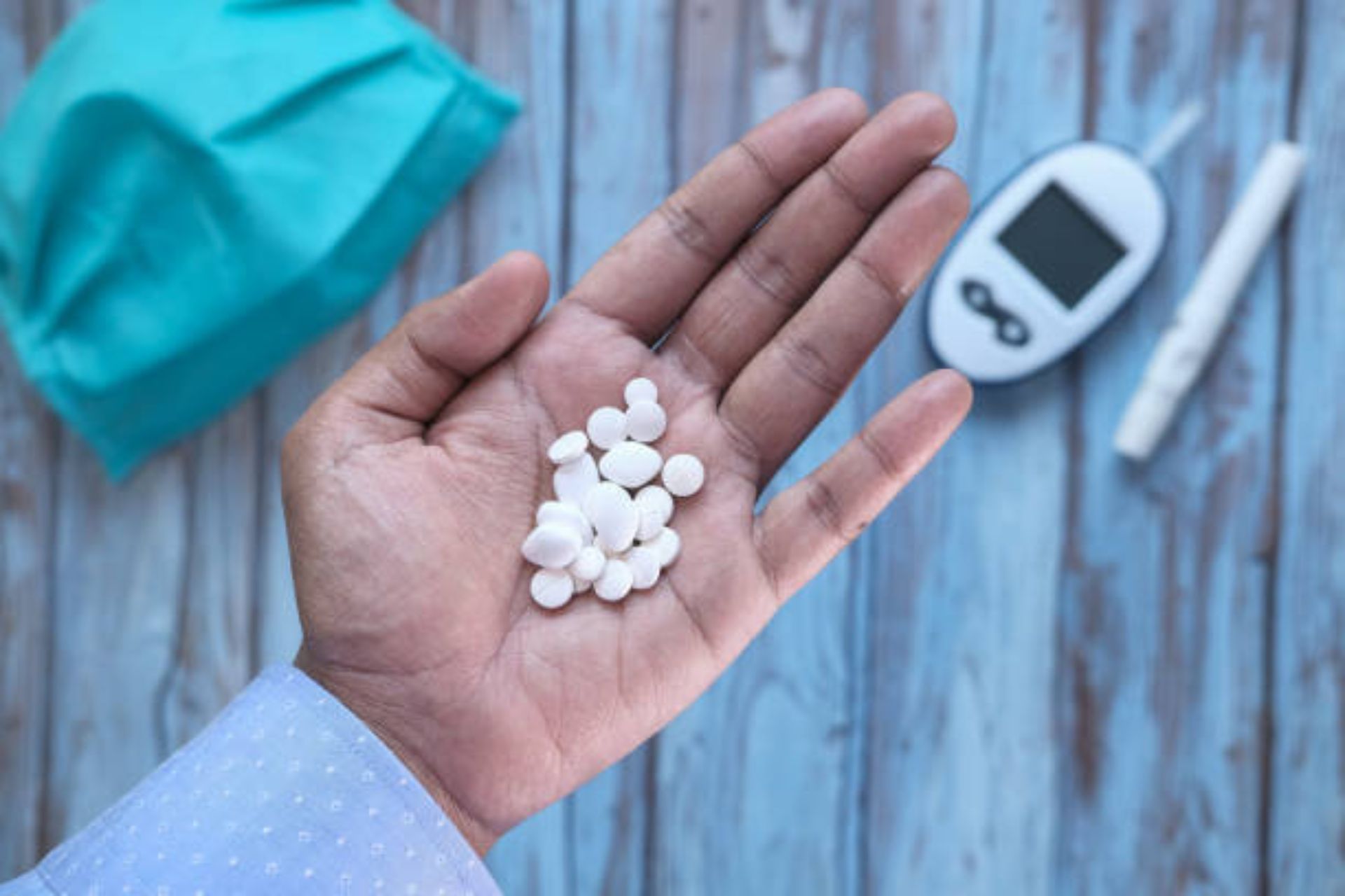 Hand holding white pills with glucometer and diabetes testing kit in background