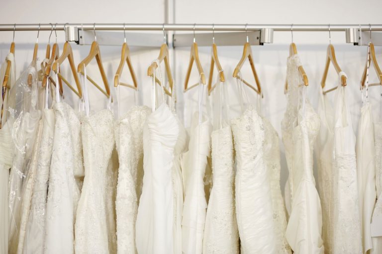 Row of white bridal gowns hanging on wooden hangers in a boutique.