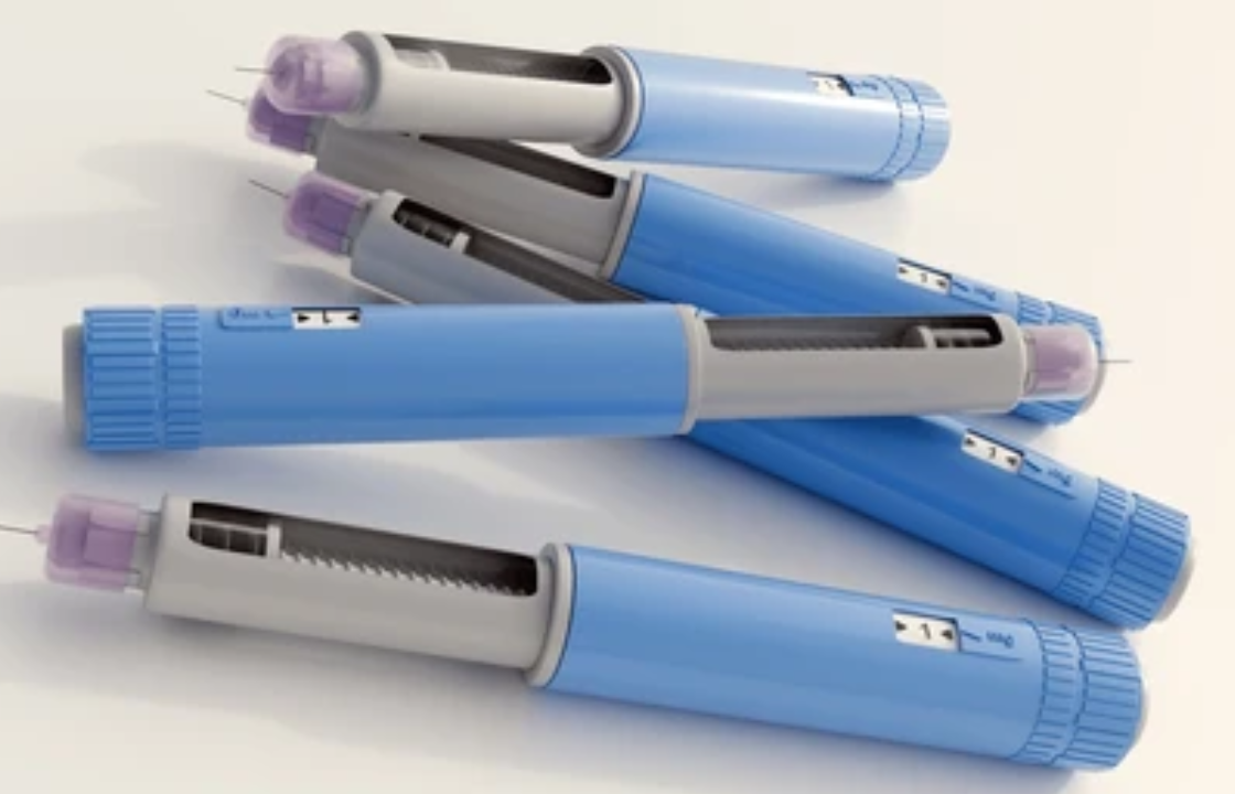 Close-up of several blue GLP-1 injection pens arranged on a light background.