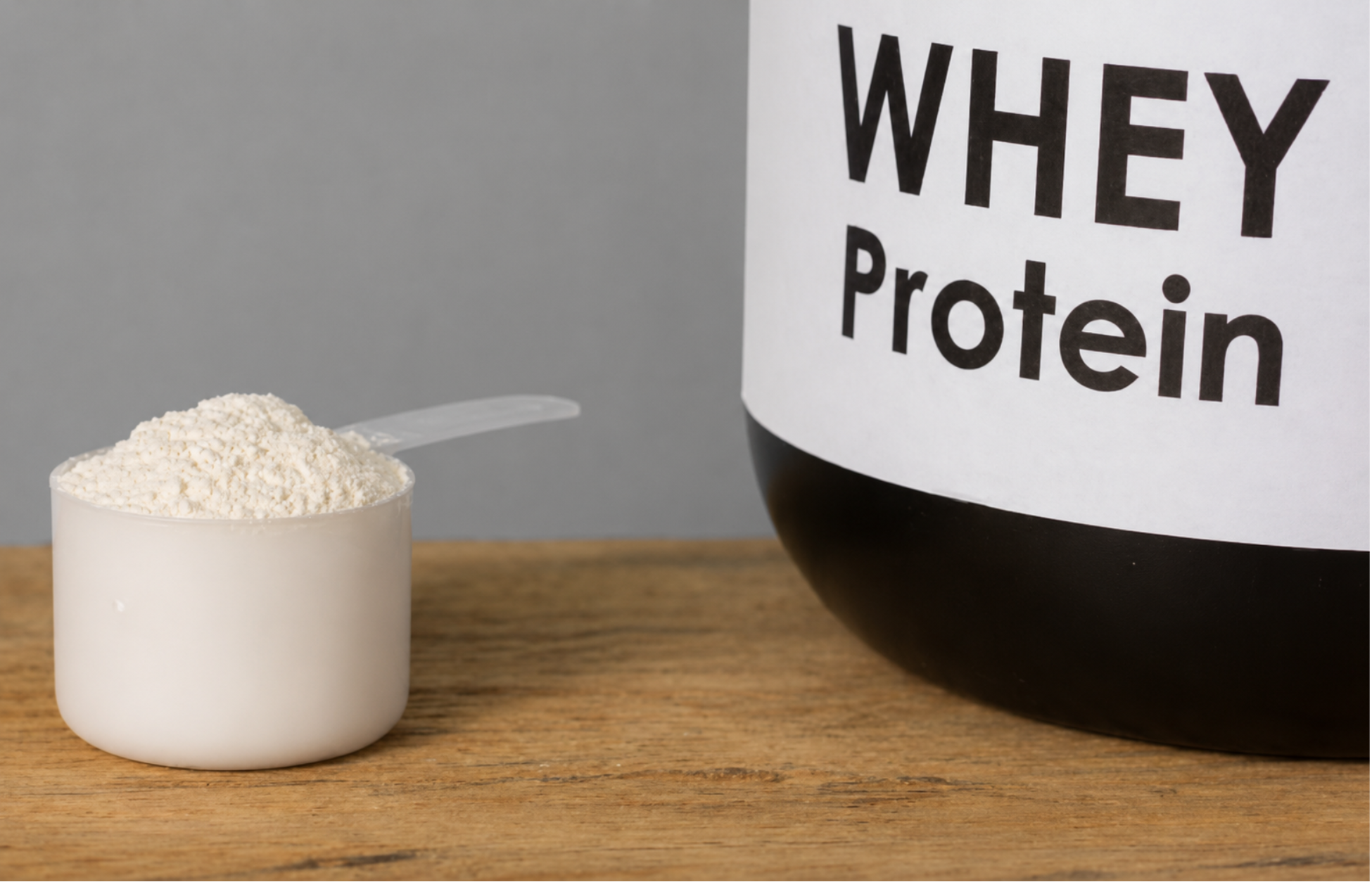 Scoop of whey protein powder beside a labeled container on a wooden surface