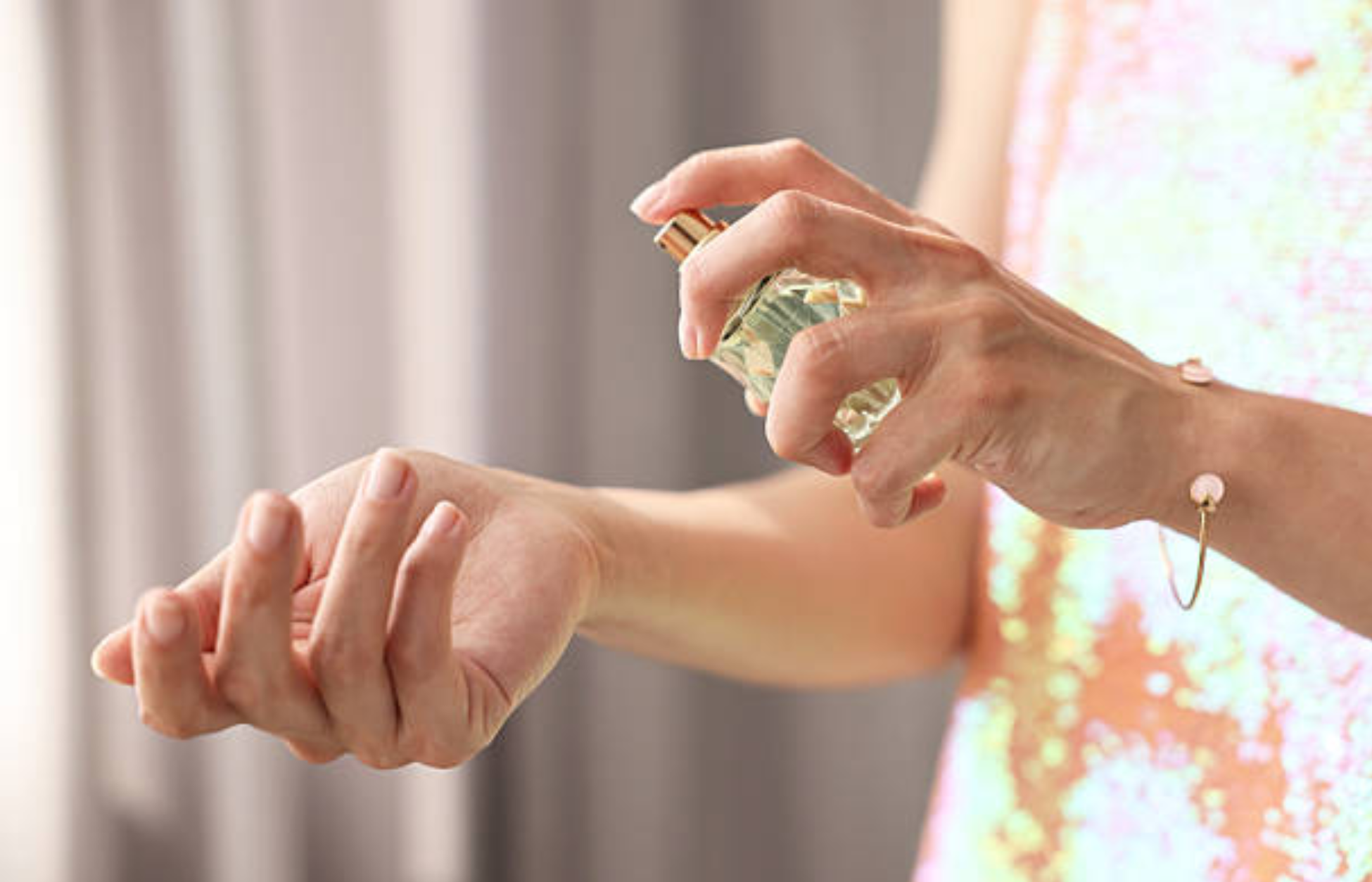 Close-up of a person spraying perfume onto their wrist in soft natural lighting.