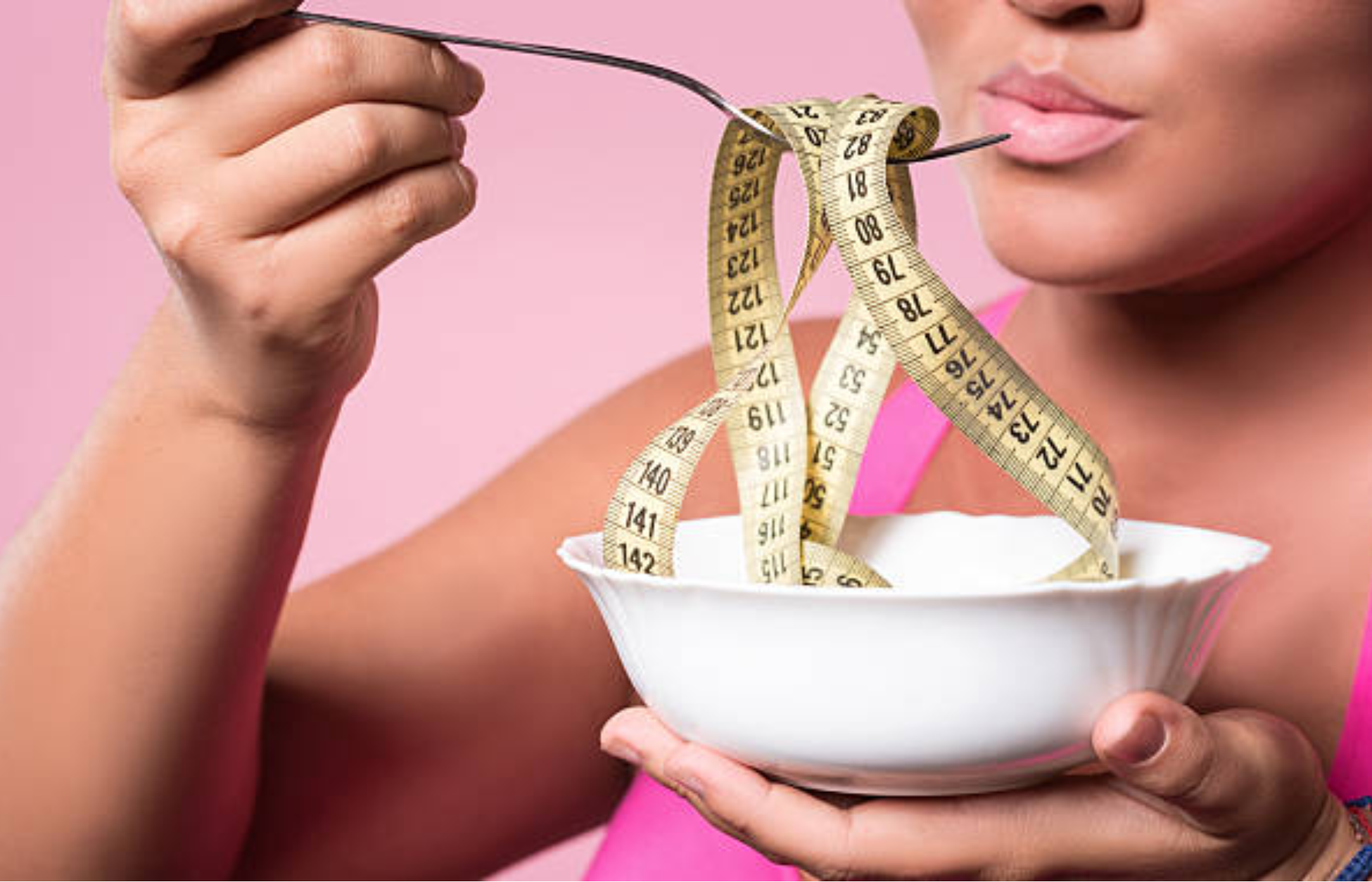 Person holding a bowl with a measuring tape wrapped around a fork, symbolizing dieting, appetite control, and weight loss.