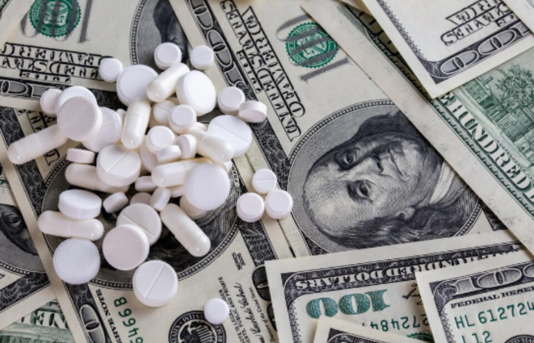 White pills scattered over U.S. dollar bills symbolizing rising pharmaceutical costs and pricing pressure.