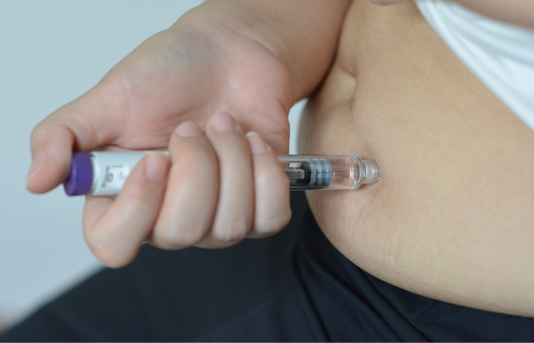 Person injecting a GLP-1 weight loss medication into their upper thigh using a prefilled pen injector.