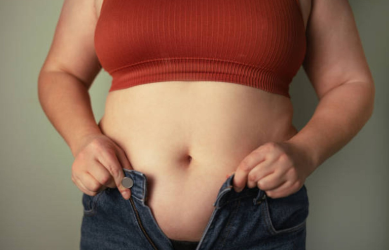 Person holding unbuttoned jeans around the waist, highlighting weight and obesity concerns.