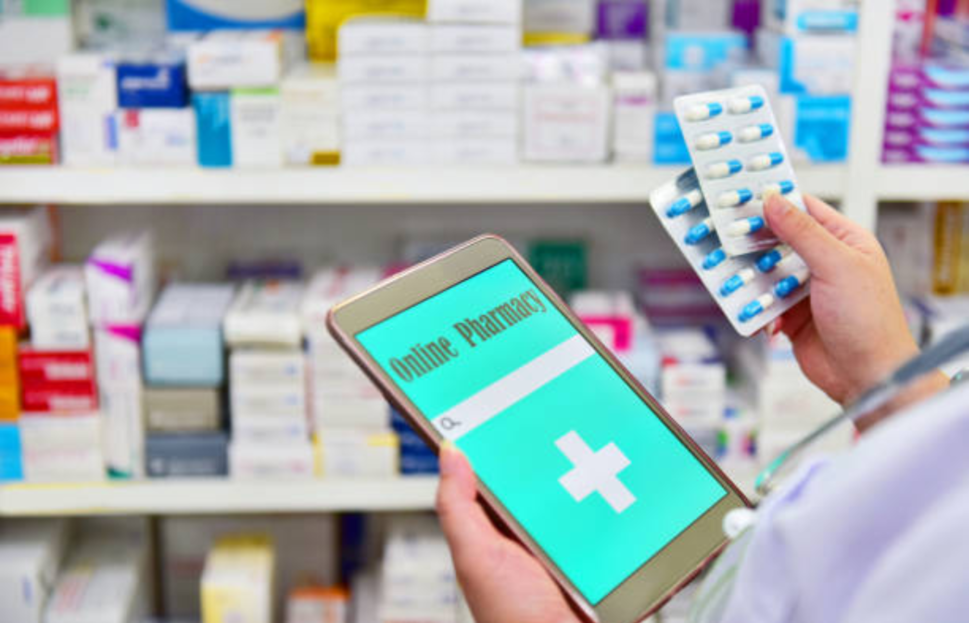 Person holding a smartphone displaying an online pharmacy app while carrying prescription medication in a pharmacy setting.