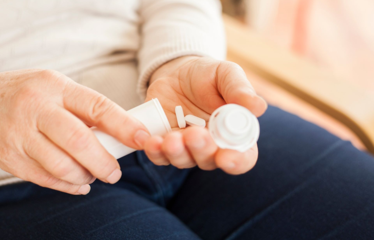 Person holding white pills from a medicine container in hand.