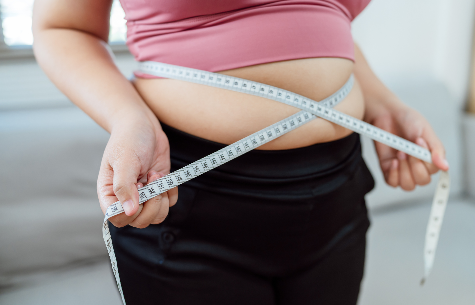 Person measuring waist with tape measure.