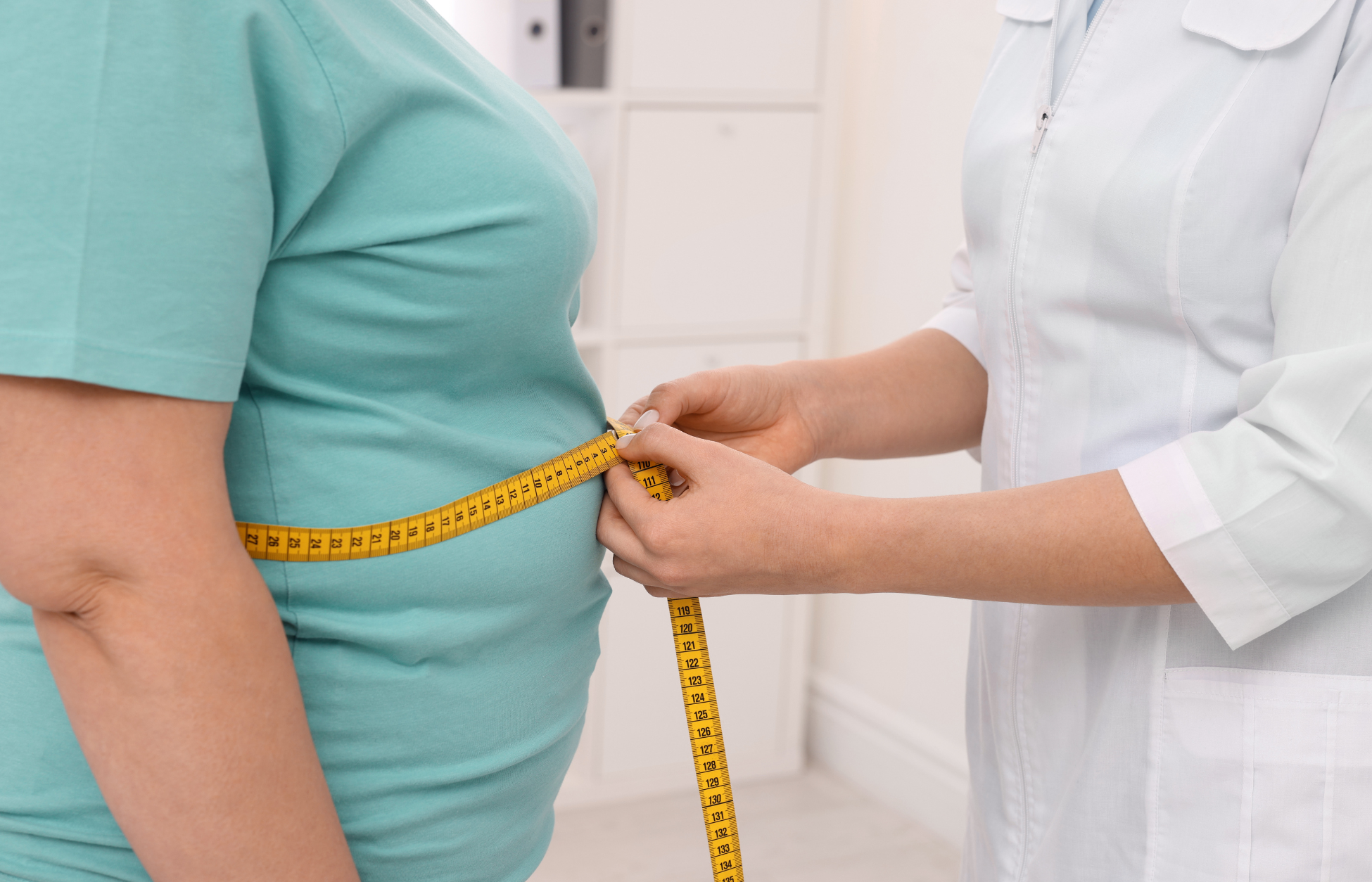 Healthcare professional measuring the waist of an overweight person with a yellow tape measure during a medical checkup.