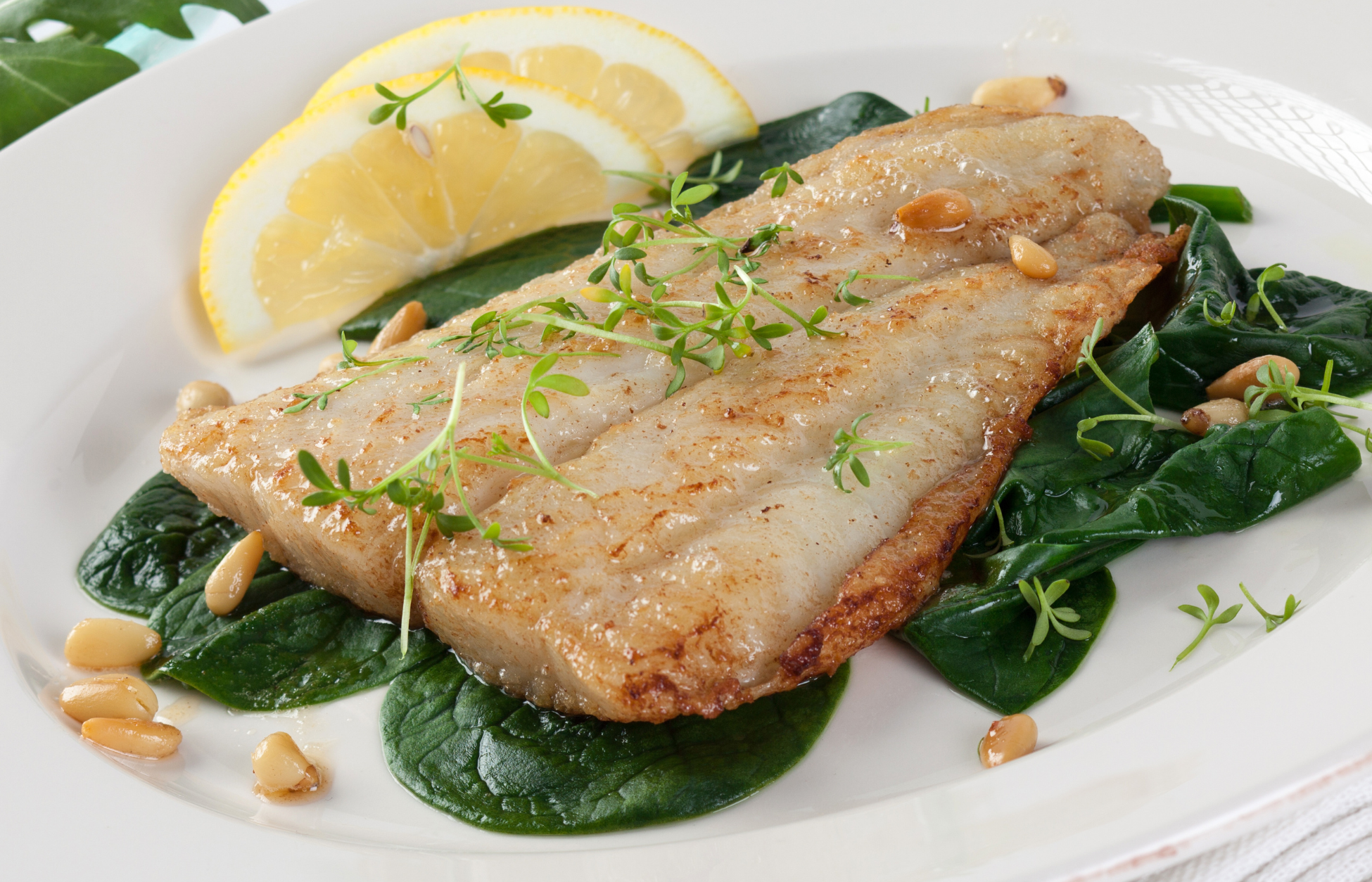 Pan-seared white fish fillets served on fresh spinach with lemon wedges, herbs, and toasted pine nuts.