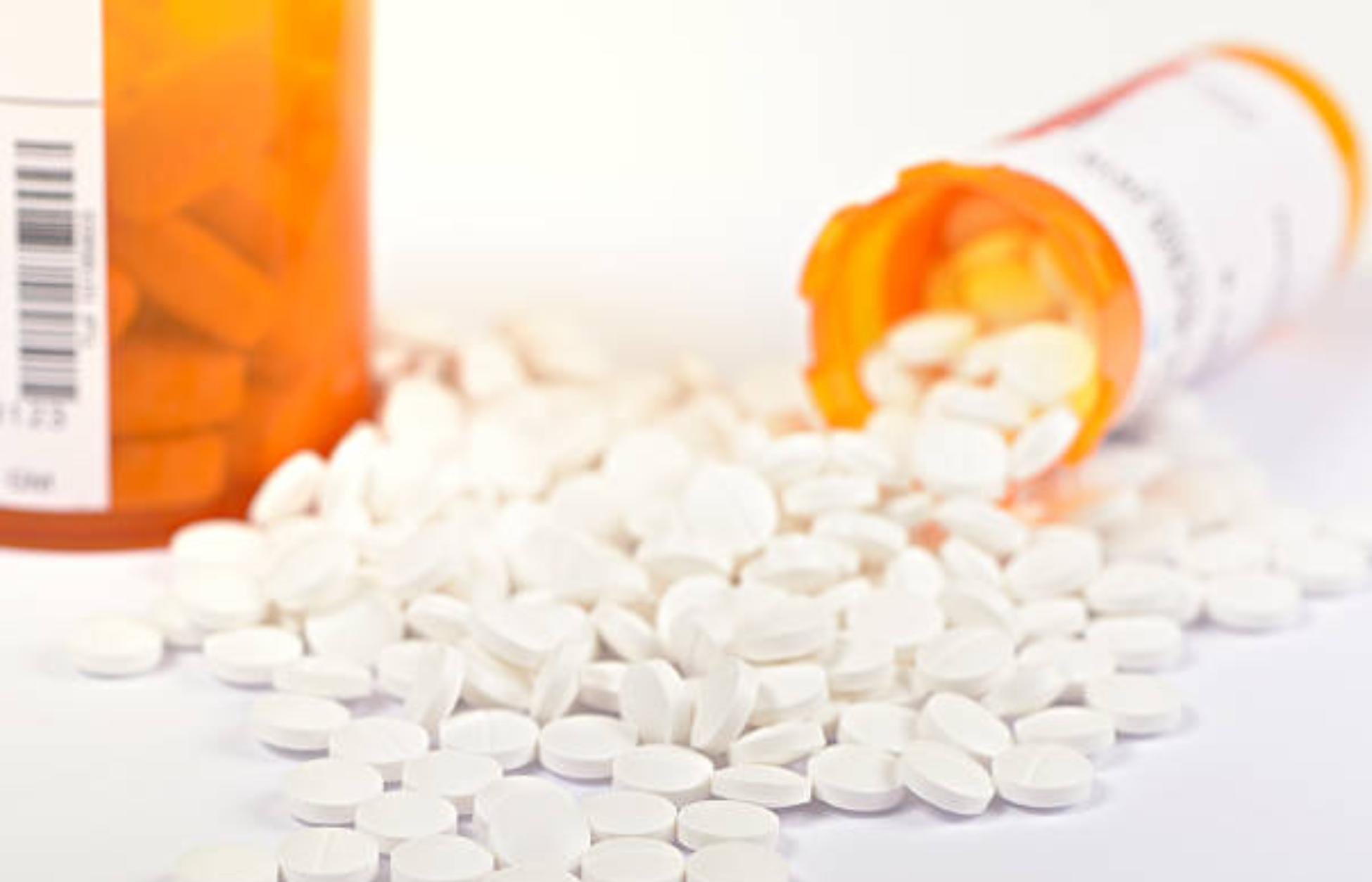 White prescription tablets spilled from orange pill bottles on a clean white surface.