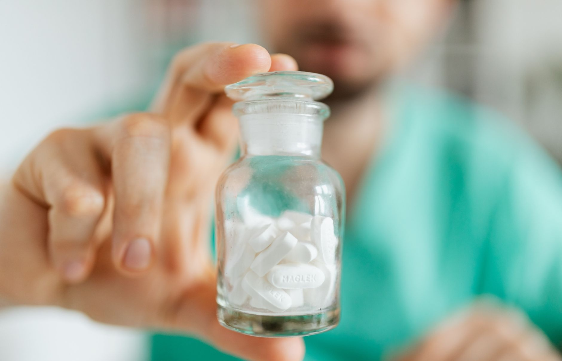 Close-up of a person holding a glass bottle filled with white tablets.