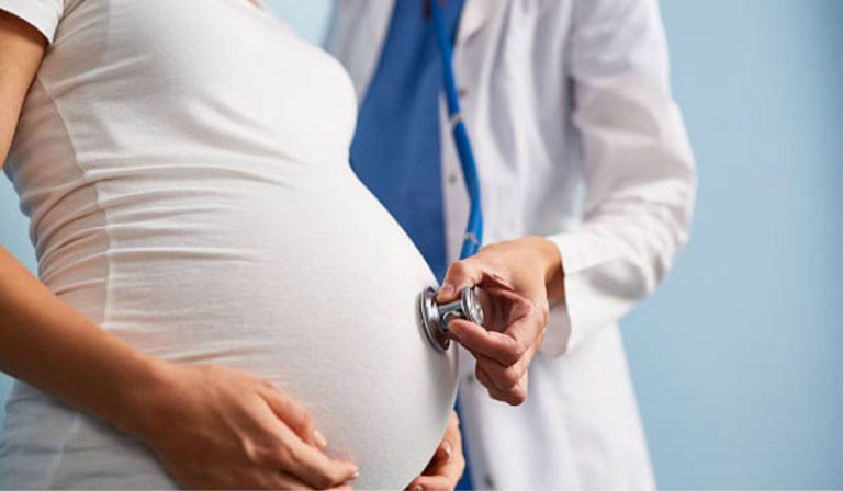 Pregnant woman undergoing a prenatal checkup while a healthcare professional listens to the baby's heartbeat with a stethoscope.