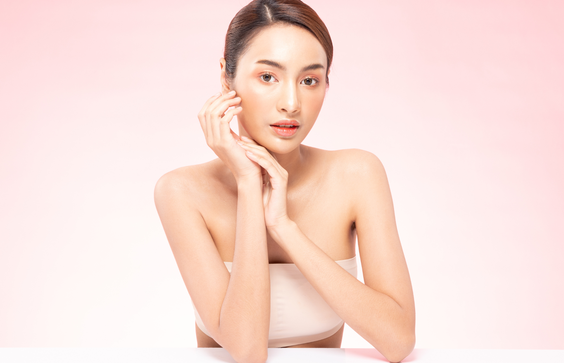 Young woman with clear, glowing skin posing against a soft pink background, highlighting skincare and skin health.