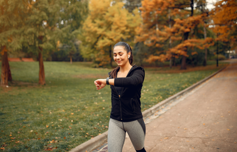 Woman walking in a park while checking her fitness tracker during an outdoor exercise session.