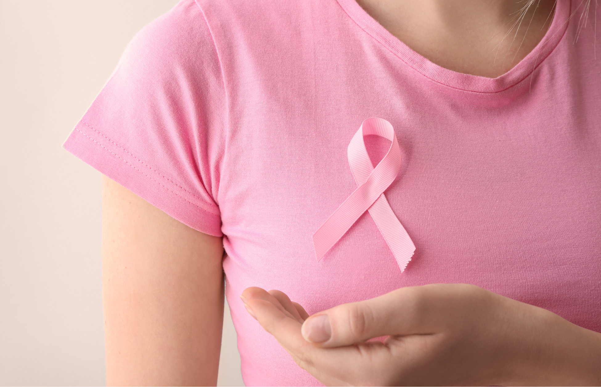 Person wearing a pink shirt with a pink breast cancer awareness ribbon pinned to the chest, symbolizing breast cancer awareness and support.
