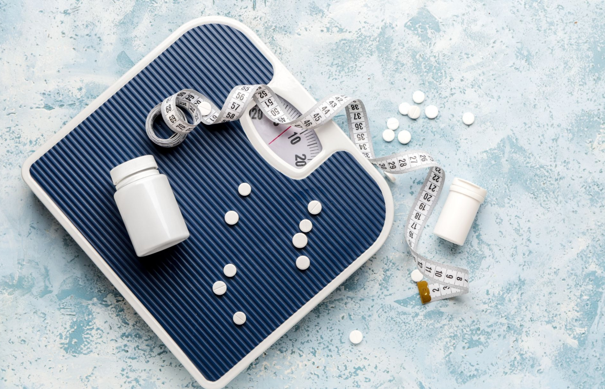 Weight-loss pills, a measuring tape, and a bathroom scale symbolizing GLP-1 medications and weight management.