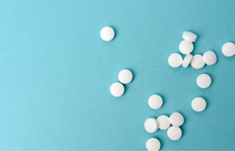 White round tablets scattered across a light blue background, representing oral medication, pharmaceutical treatment, or healthcare concepts.