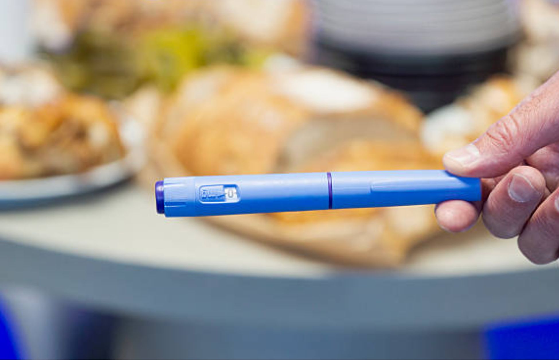 Person holding a GLP-1 injection pen with food blurred in the background.
