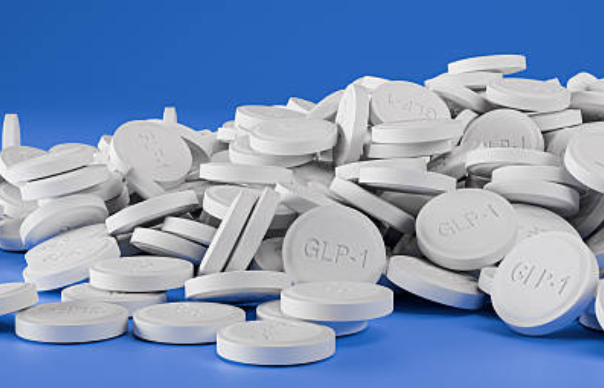 White GLP-1 tablets piled on a blue background, representing the growing market for obesity and diabetes medications.