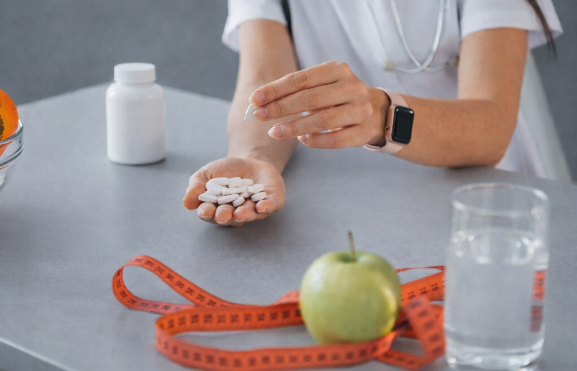 Healthcare professional holding oral GLP-1 tablets with a measuring tape, apple, and water, representing weight management treatment.